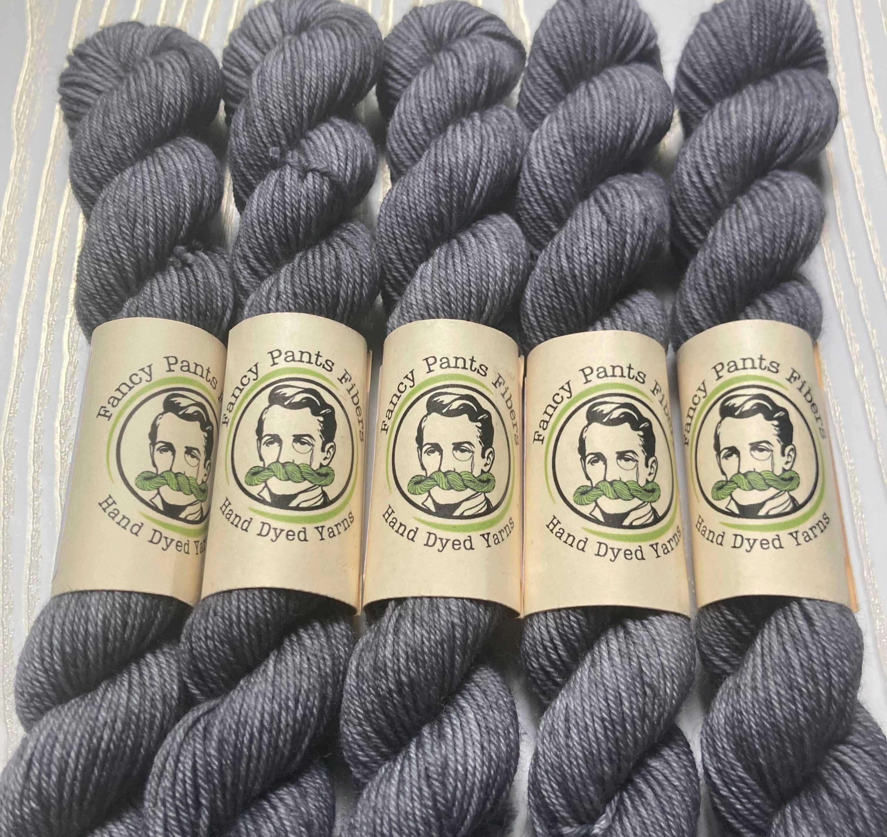 Five skeins of gray yarn with 'Fancy Pants Yarns' labels on a textured background