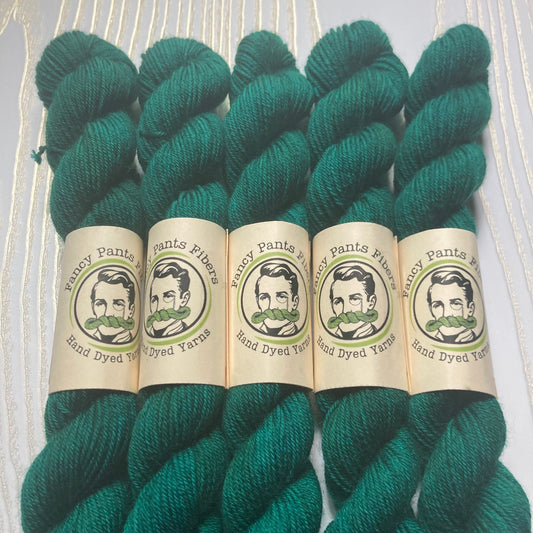 Five mini skeins of teal yarn with labels on a light wooden background